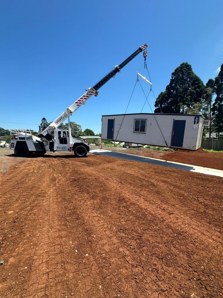 A crane working on red dirt, lifting a modular home. Northern Rivers, NSW